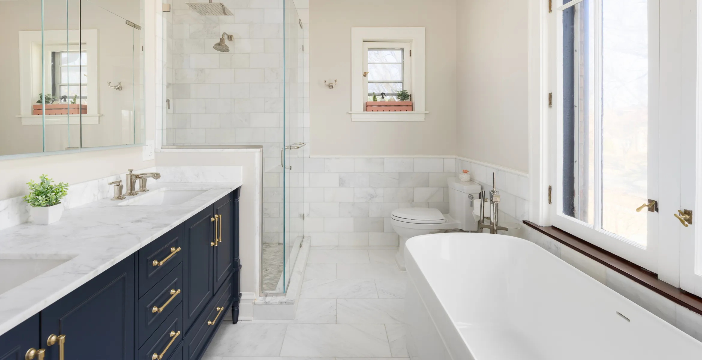 Luxury bathroom addition in Dallas TX featuring a freestanding soaking tub, marble tile shower, navy double vanity, and custom brass fixtures