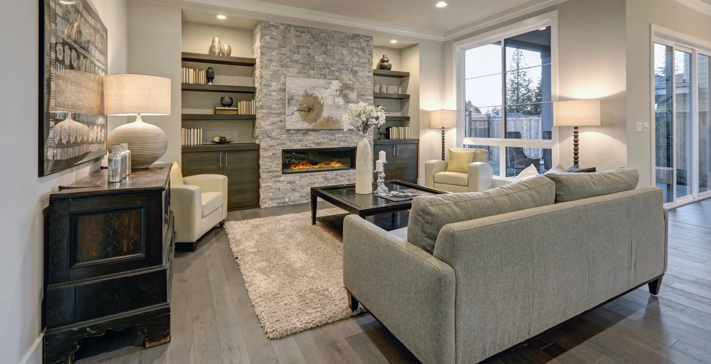 Custom family room and great room addition in Dallas TX featuring a stone fireplace wall, built-in shelving, layered lighting, and a warm open-concept seating layout