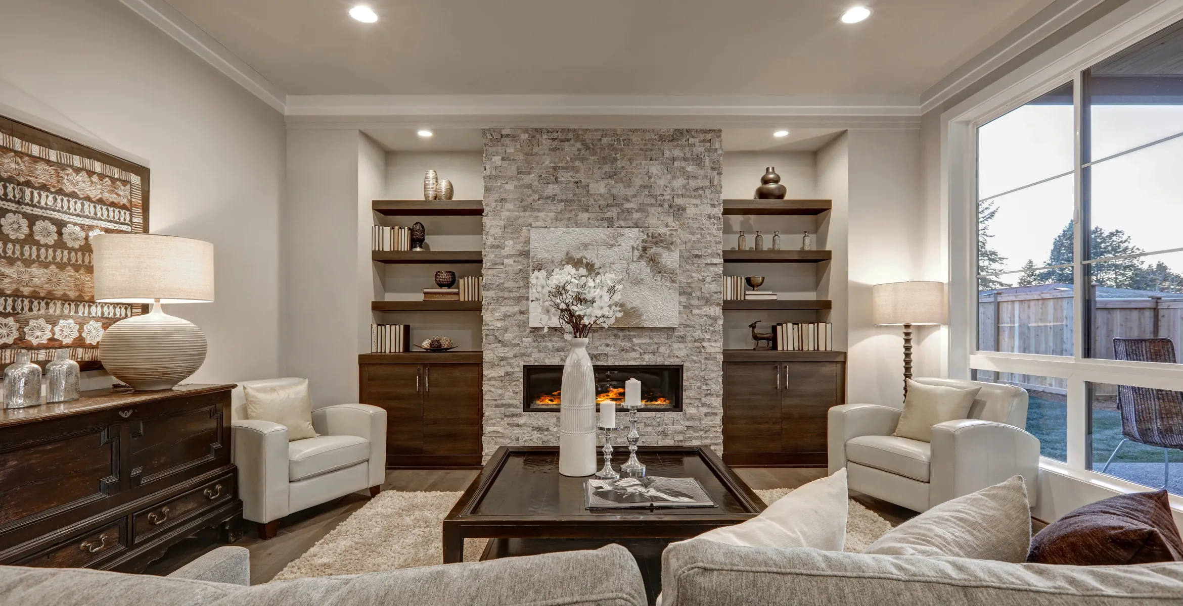 Luxury great room addition in Dallas TX with floor-to-ceiling stone fireplace, symmetrical built-in cabinetry, expansive windows, and elegant family gathering space